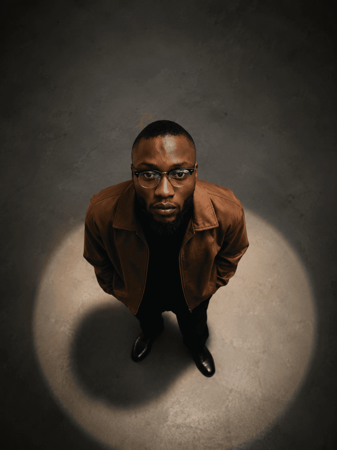 Olatunji Oluwashola standing in a spotlight, looking up at the camera
