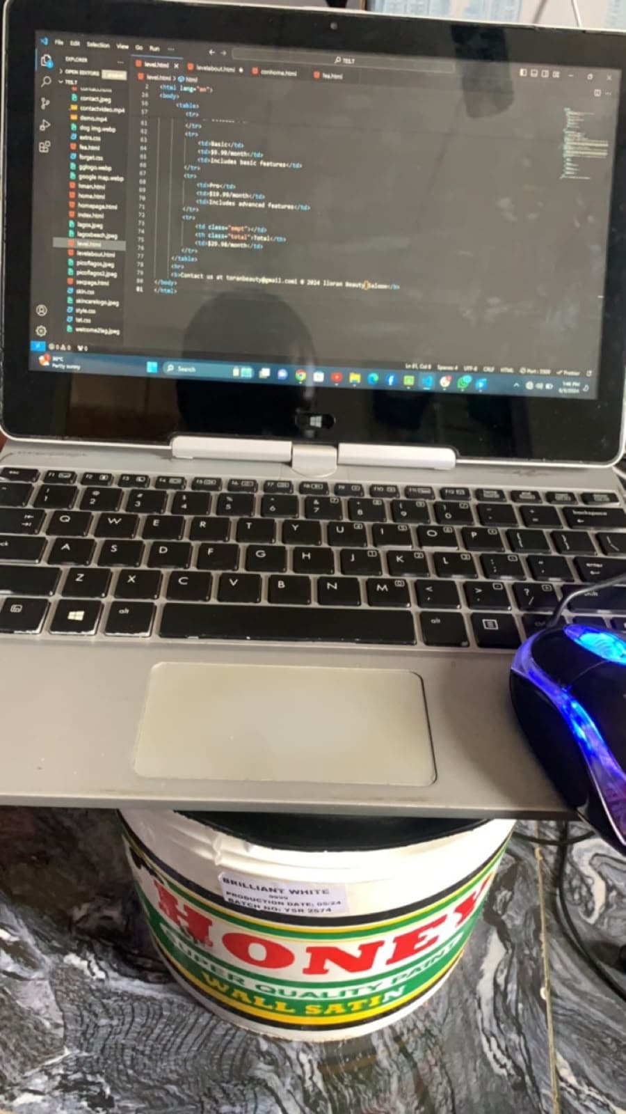 An old laptop propped on a bucket of wall paint, a code editor open on the screen